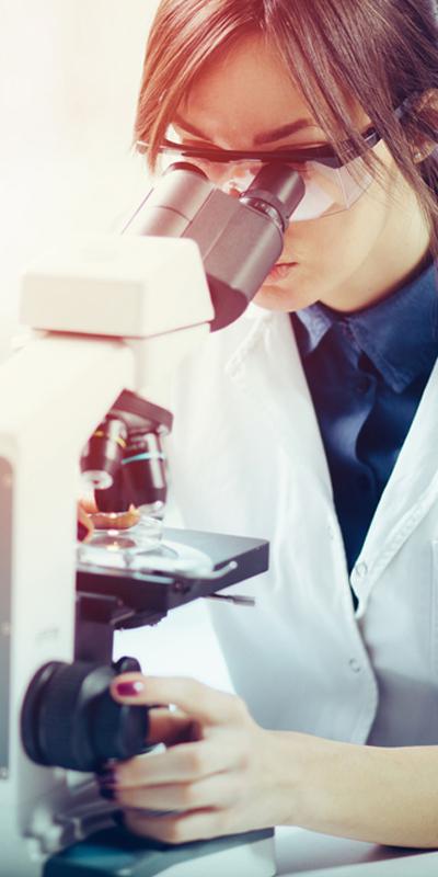 Woman wearing a scientist's white coat, looking into a microscope